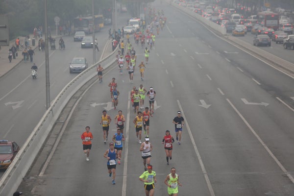 Marathon participants on a closed highway run through smoggy air