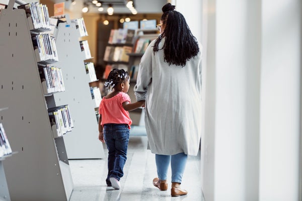 Rear view of a father and a small child holding hands, walking through a public library