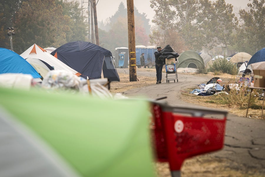 A Camp Fire victime pushes a shopping cart with donated items passed tents in an evacuation camp set up in Chico, California, U.S., on Thursday, Nov. 15, 2018