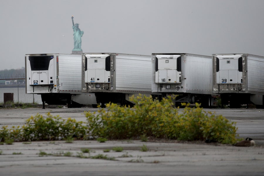 The Statue of Liberty is seen behind a row of refrigerator trucks