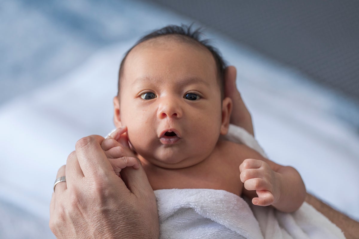 Close up photo of a one week old baby boy with dark hair and eyes open
