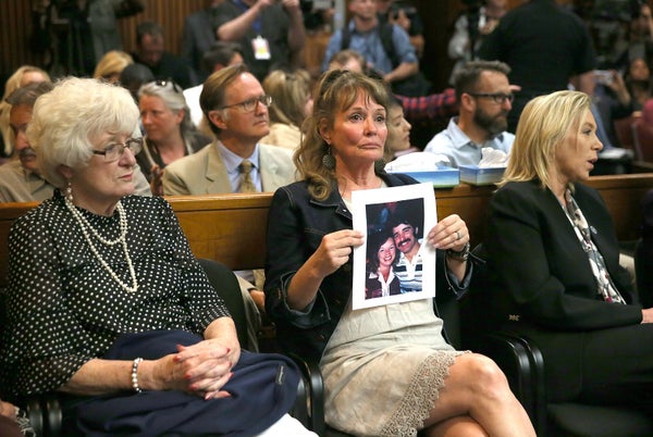 A seated woman in a courtroom holds a photo of family members