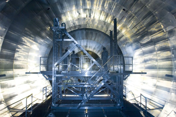 3 people in blue suits inside a neutrino detector behind a blue metal platform