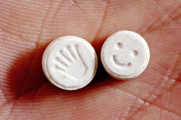 Close up photograph of 2 MDMA or ecstasy pills in a person's hand. One pill has a crown graphic stamped into it, the other has a smiley face