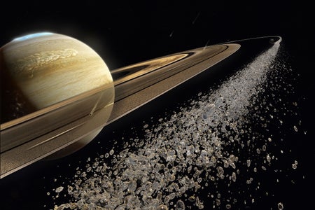 A close-up of small particles of ice and rock within a ring of Saturn, which looms in the background.