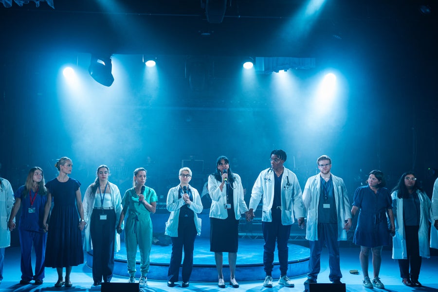 The Lifeline chorus of real-life scientists and health care professionals on stage holding hands.