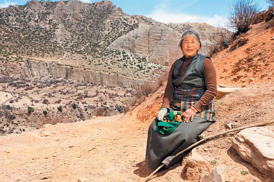 Native Tibetan woman sitting outside in traditional clothing.
