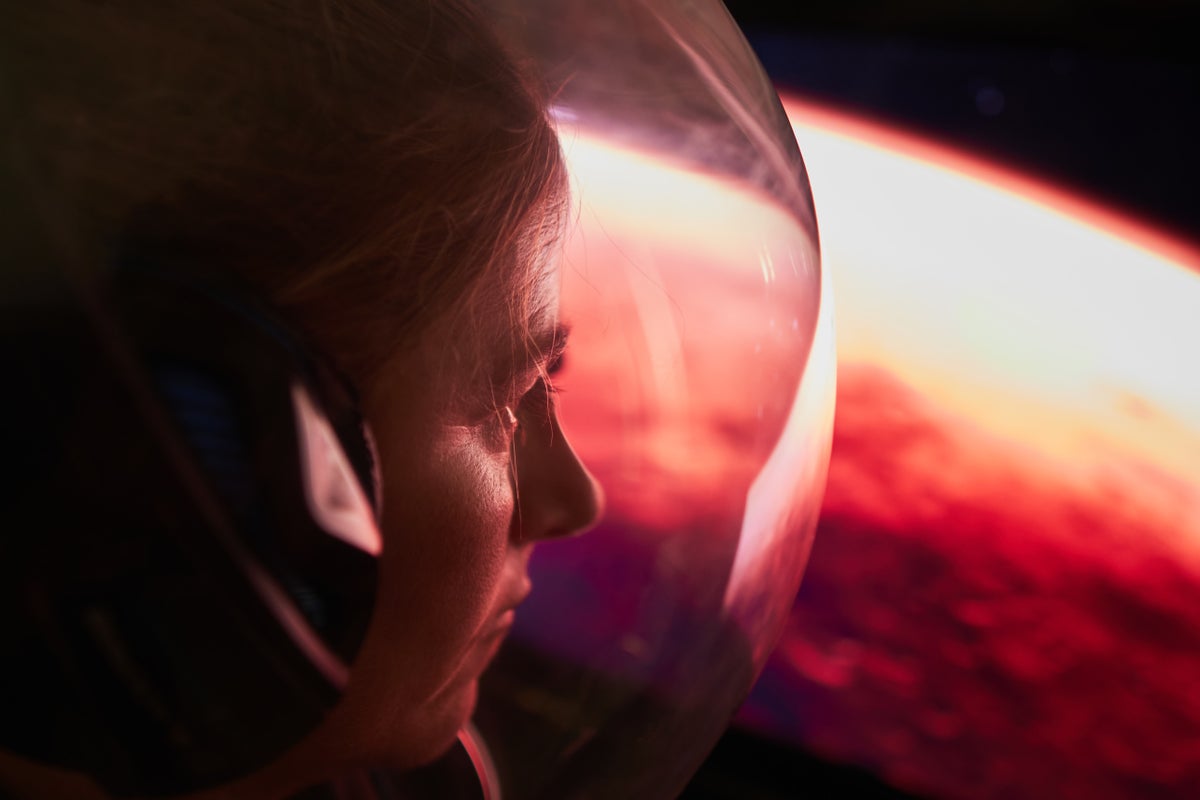 An astronaut looks out on a red planet.