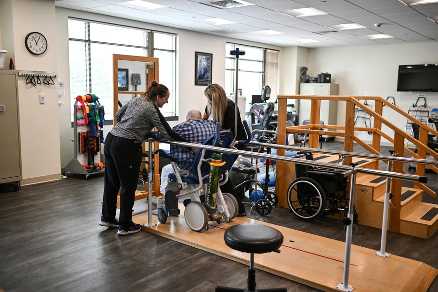 Therapists assist an older man with therapy in the extended care facility