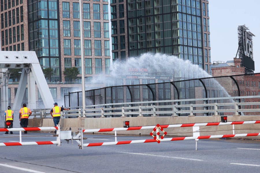 Transportation workers stand on the Third Avenue Bridge in New York City, which was stuck open by high temperatures on July 8, 2024, as a stream of water is sprayed onto the bridge in an attempt to lower its temperature