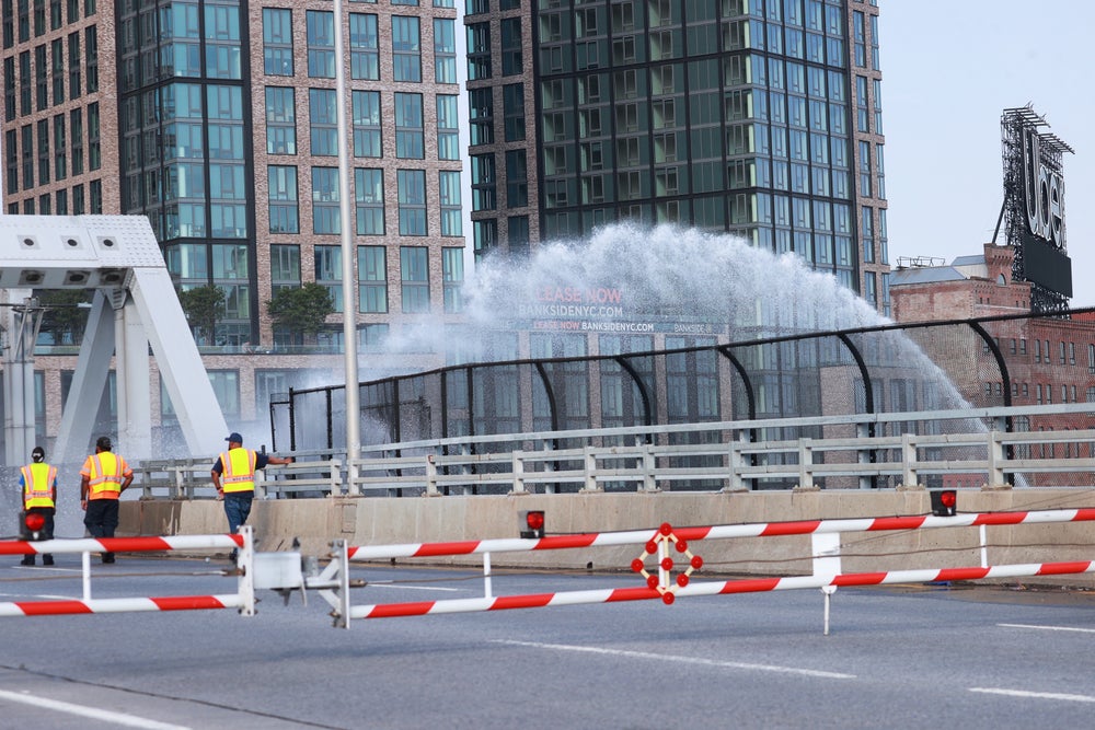 Los trabajadores del transporte se encuentran en el puente de la Tercera Avenida en la ciudad de Nueva York, que quedó abierto debido a las altas temperaturas el 8 de julio de 2024, mientras se rocía un chorro de agua sobre el puente en un intento de bajar su temperatura.