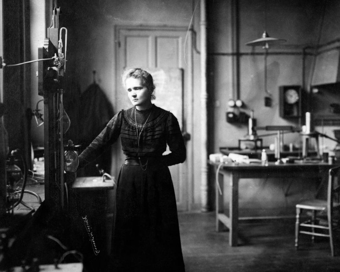 A black and white photograph showing Marie Curie standing in a science laboratory.