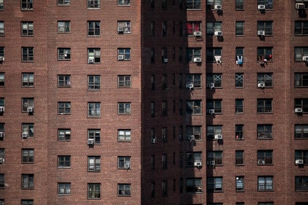 Brick building with small windows some with Air Conditioners and others with clothes hanging outside.