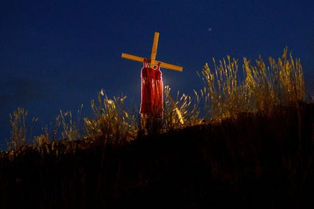 A night photo showing an illuminated cross with red child’s dress draped over it.