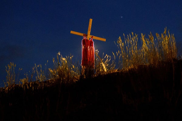 A night photo showing an illuminated cross with red child’s dress draped over it.
