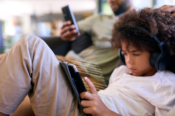 Close Up Of Father With Mobile Phone And Son Using Digital Tablet Reading With Headphones At Home