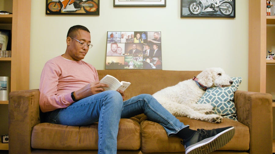 Kevin Wake sitting on a yellow couch with a golden retreiver dog, reading a book