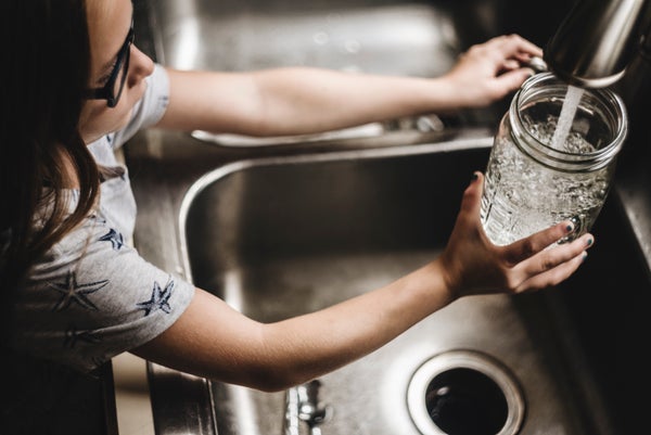 Little girl fills glass with water at kitchen sink
