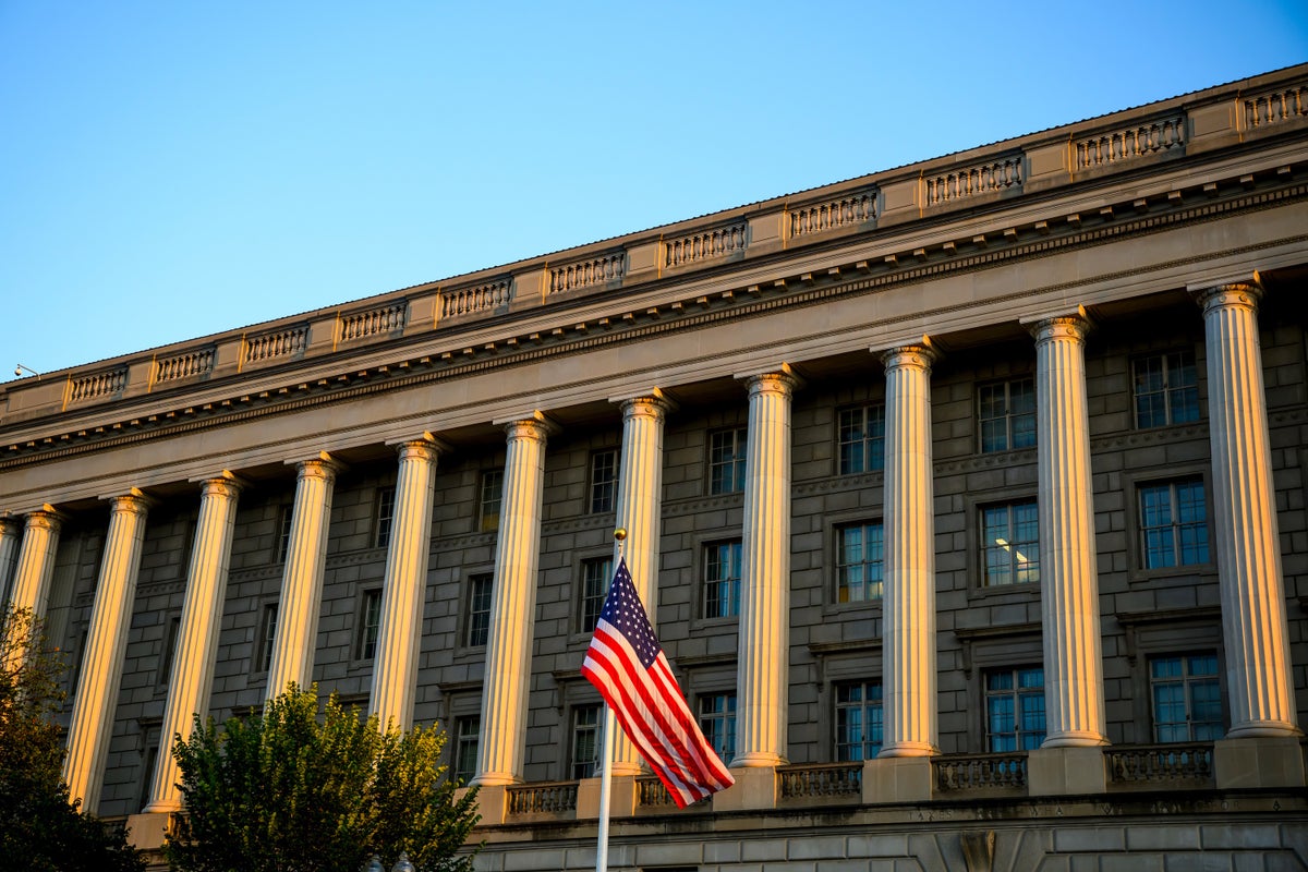 A view of the columns of a large federal office building in sunset light with a US flag waving weakly in front.