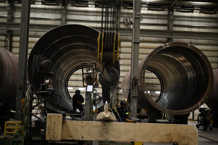 Two metal circular parts of a wind turbine with a factory worker inside left circle.