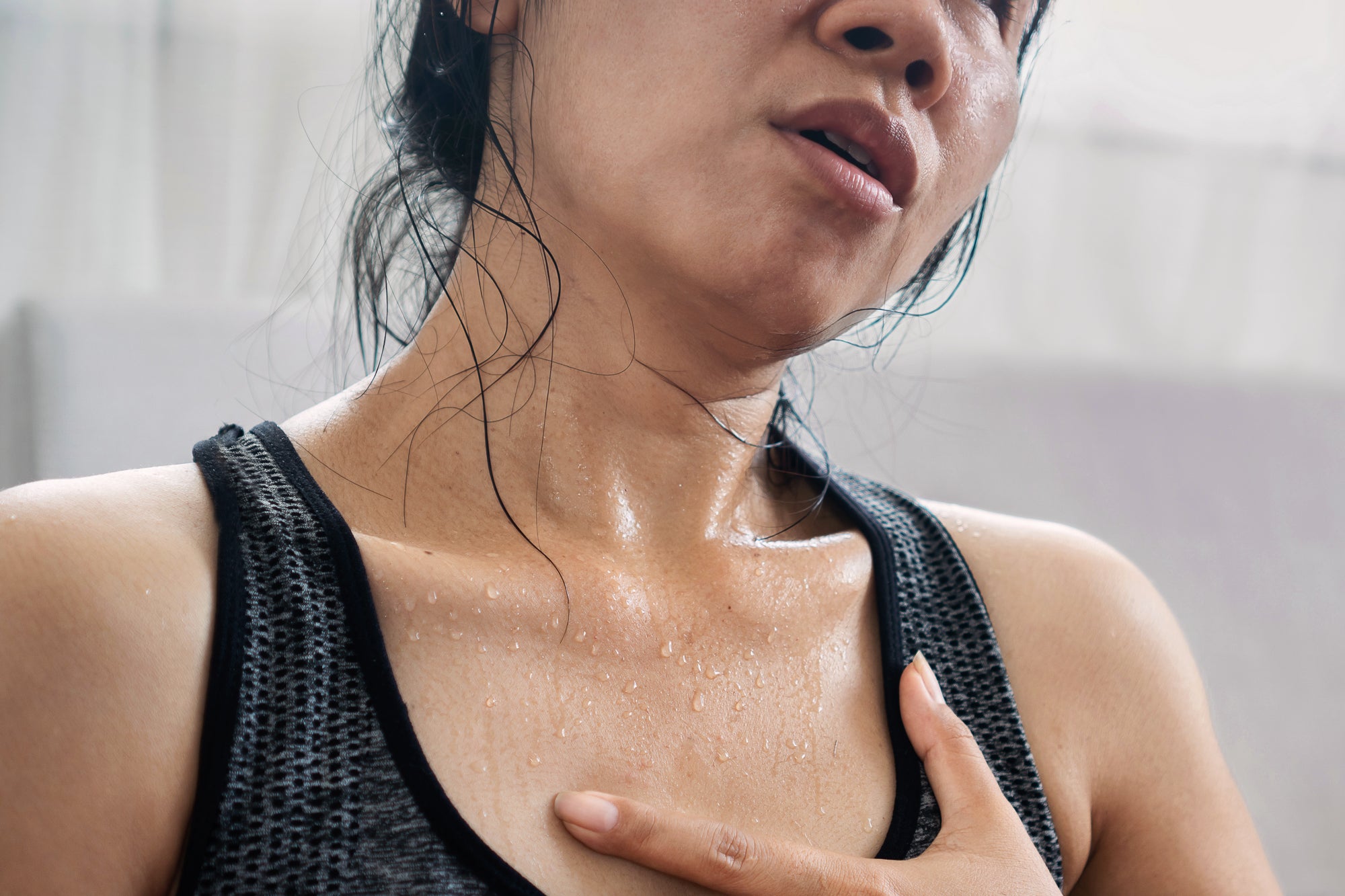 Stock photograph of Asian female model appearing to be overheated, sweating, with one hand placed on chest