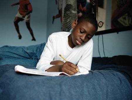 Child laying on his bed writing.