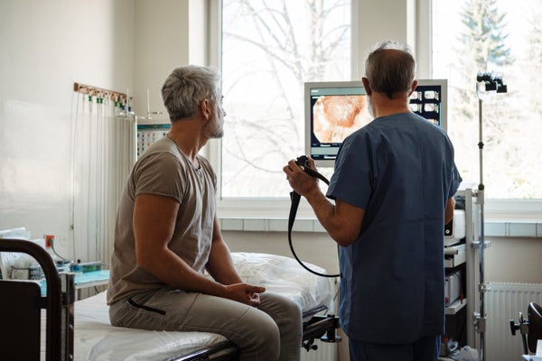 Doctor explaining colonoscopy results to patient using monitor images on screen.