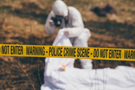 Man in white suit photographing crime scene behind police tape