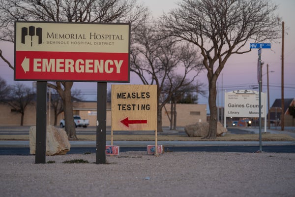 a wooden sign pointing to measles testing in a hospital parking lot