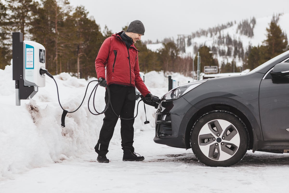 Man charging his electric vehicle in a snowy parking lot with mountains in the background