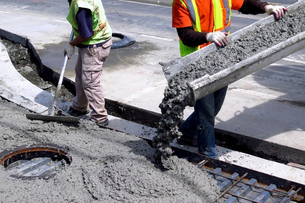 Two workers with safety jackets pouring concrete.