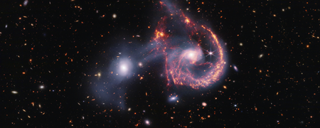 Two galaxies are shown mid-collision against a background of more distant galaxies.