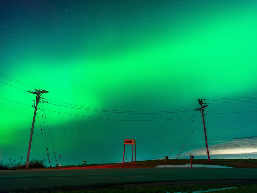 Bright green auroras across the central part of the sky with power lines in the foreground.