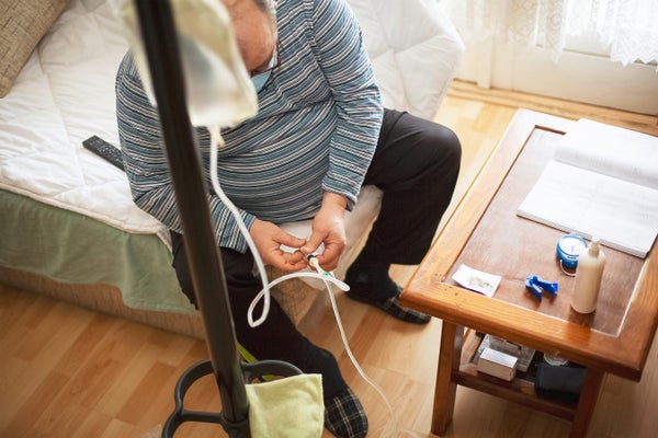 Senior man connecting peritoneal dialysis with catheter at home.