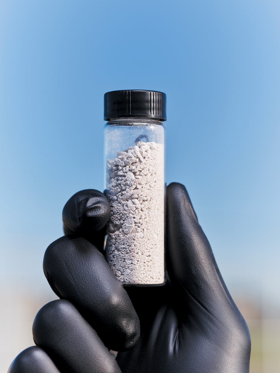 A hand in a black glove holding a small bottle of limestone