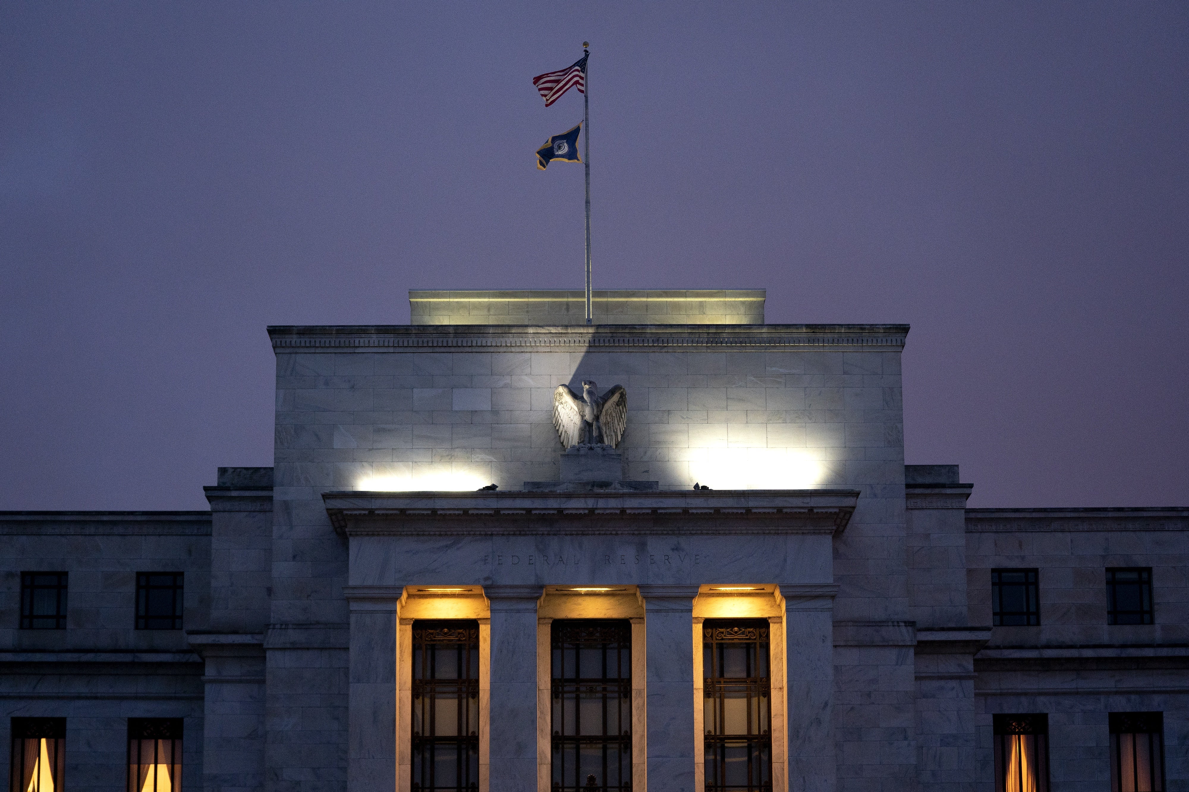 Federal Reserve Building in purple sky with US flag and 3 illuminated windows.