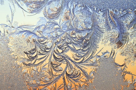 Swirls of ice coat a flat pane with orange and blue reflected light
