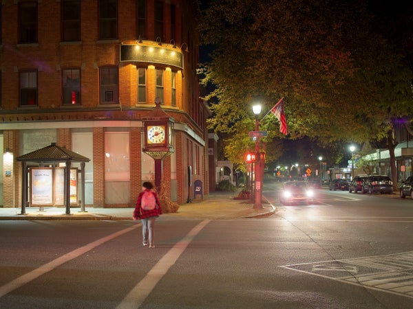 Person with backpack crosses street at night