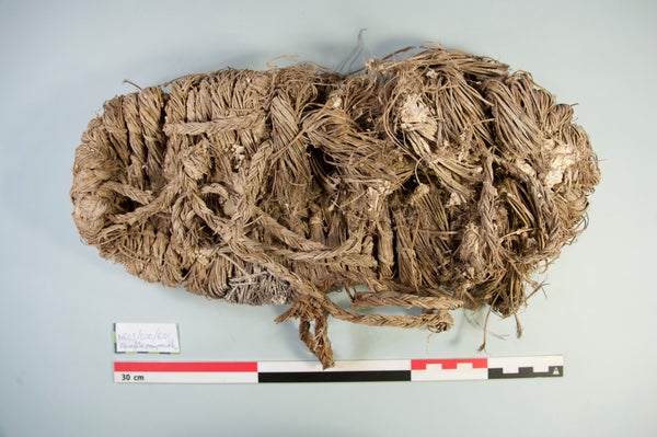 A woven grass shoe on a blank background near a 30 centimeter measuring stick.