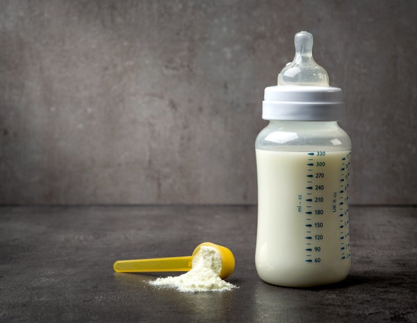 Baby bottle with a spoonful of formula on greay studio background