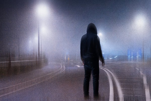 An ominous hooded figure, silhouetted against street lights on a foggy road at night
