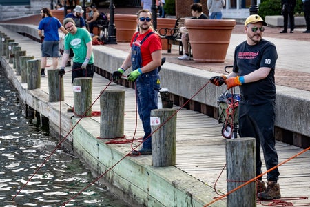 Four magnet fishers stand on a pier while pulling their lines in from the water