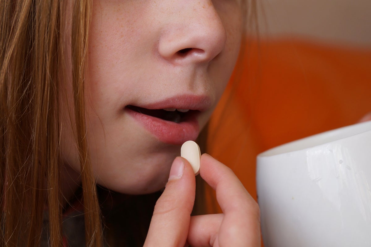 Close up of a teenager taking a prescription pill, holding the pill in front of their mouth