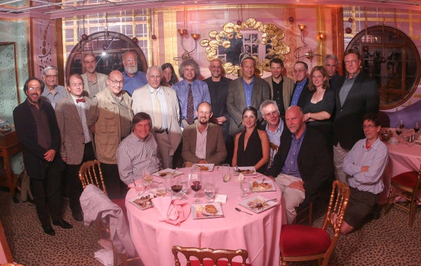 A group of men and women seated and standing for a group photograph in front of a round pink table.