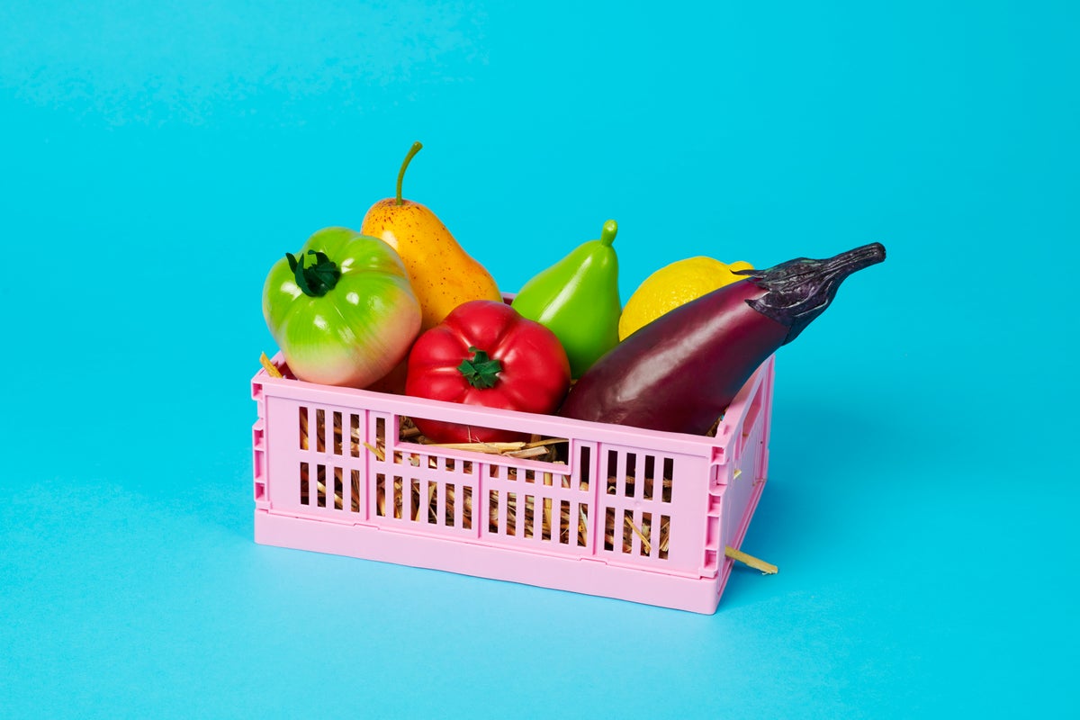Plastic fruits and vegetables in a pink crate on a blue background