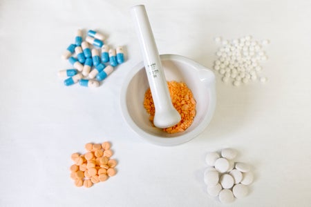 mortar and pestle with an orange powder inside. surrounding it are other pills of various colors and sizes