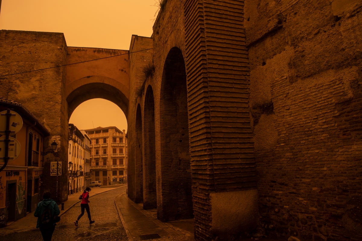 A woman walks across the street in Granada, where Saharan dust has turned the sky orange.