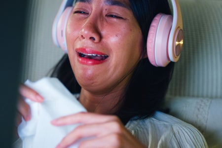 Closeup of young woman on bed wearing headphones and crying while watching movie