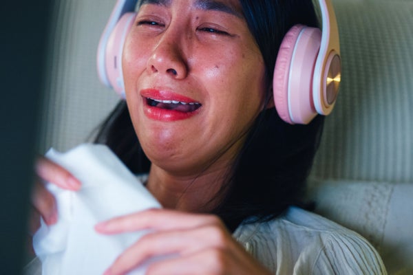 Closeup of young woman on bed wearing headphones and crying while watching movie