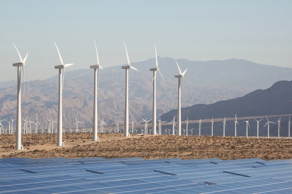 Solar panels and wind turbines in the California desert with mountains in the background.